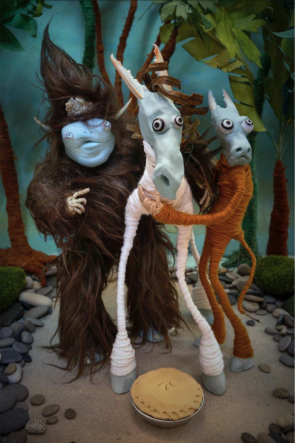 3 stop motion characters, a furry monster with horns, a bipedal cow and a horse offer a pie to the forest spirit.