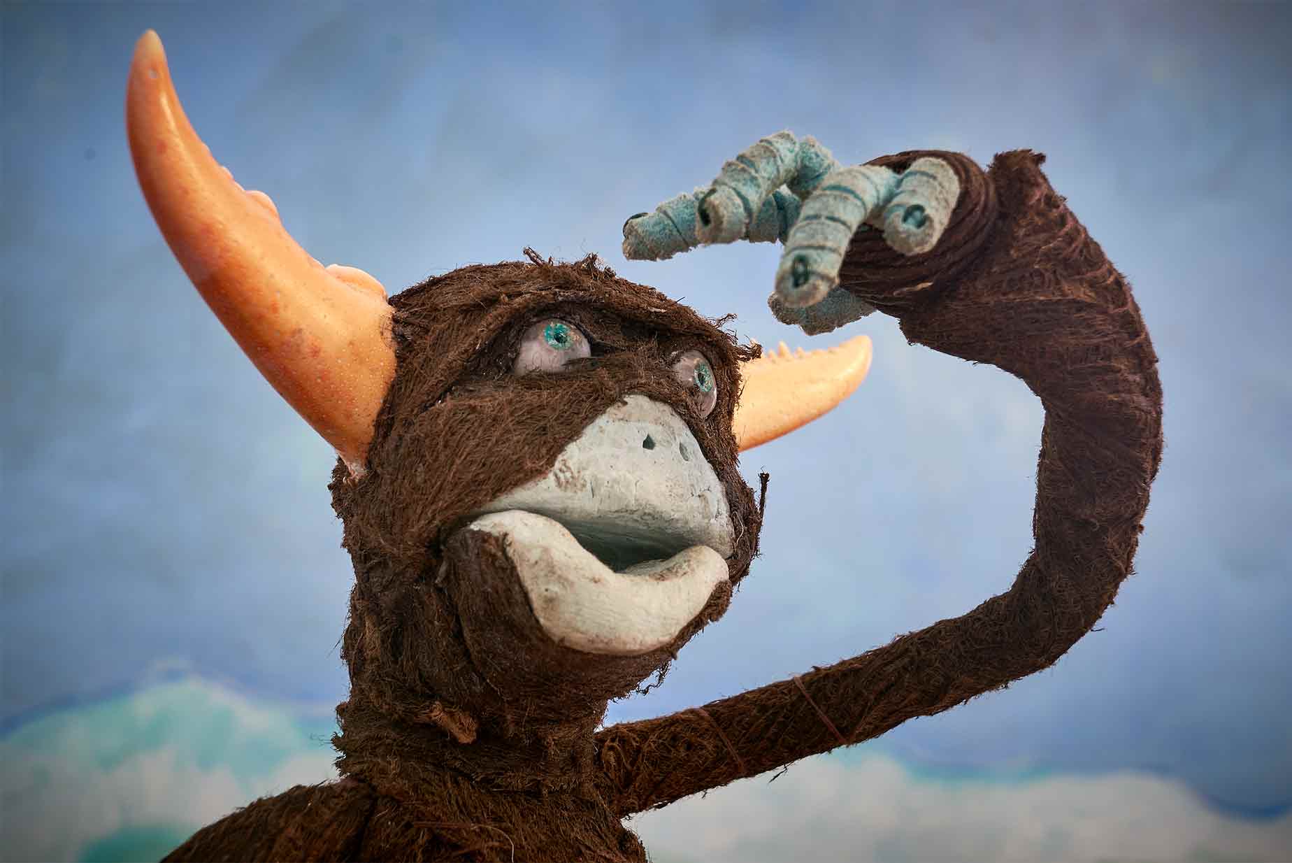 A stop motion character looks out over the landscape in search of something. The character's face is made with air-dry clay and covered in bark cloth. He has horns.
